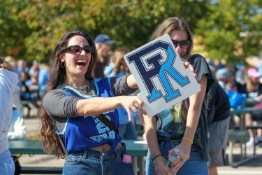 Female alum holding up a RI sign